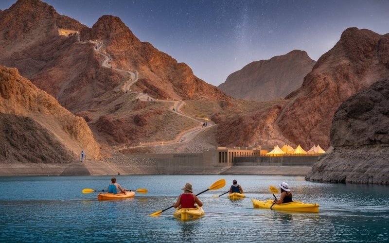 People kayaking on a serene blue lake surrounded by rocky mountains during a Hatta tour from Dubai.