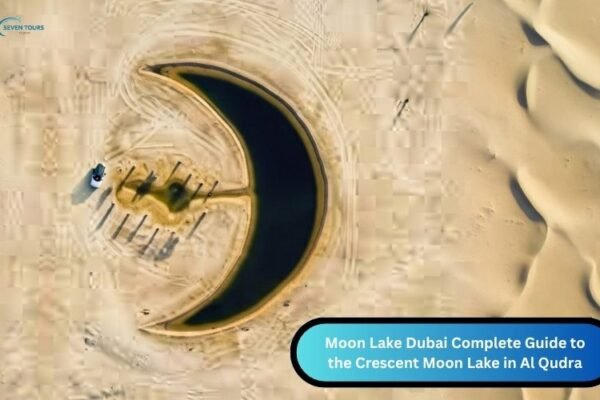 Moon-Lake-Dubai Aerial view of the crescent shaped Moon Lake in Dubai’s Al Qudra Desert, surrounded by sand dunes with a few palm trees and vehicles nearby.