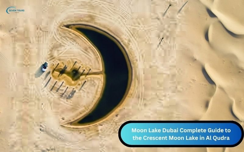 Aerial view of the crescent shaped Moon Lake in Dubai’s Al Qudra Desert, surrounded by sand dunes with a few palm trees and vehicles nearby.