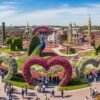 Visitors exploring colorful floral sculptures, heart-shaped arches, and peacock displays at Dubai Miracle Garden – miracle garden dubai sightseeing tour